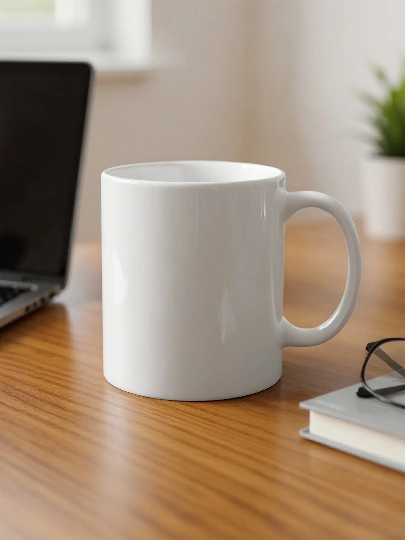 White ceramic mug on a wooden desk with a laptop and glasses.