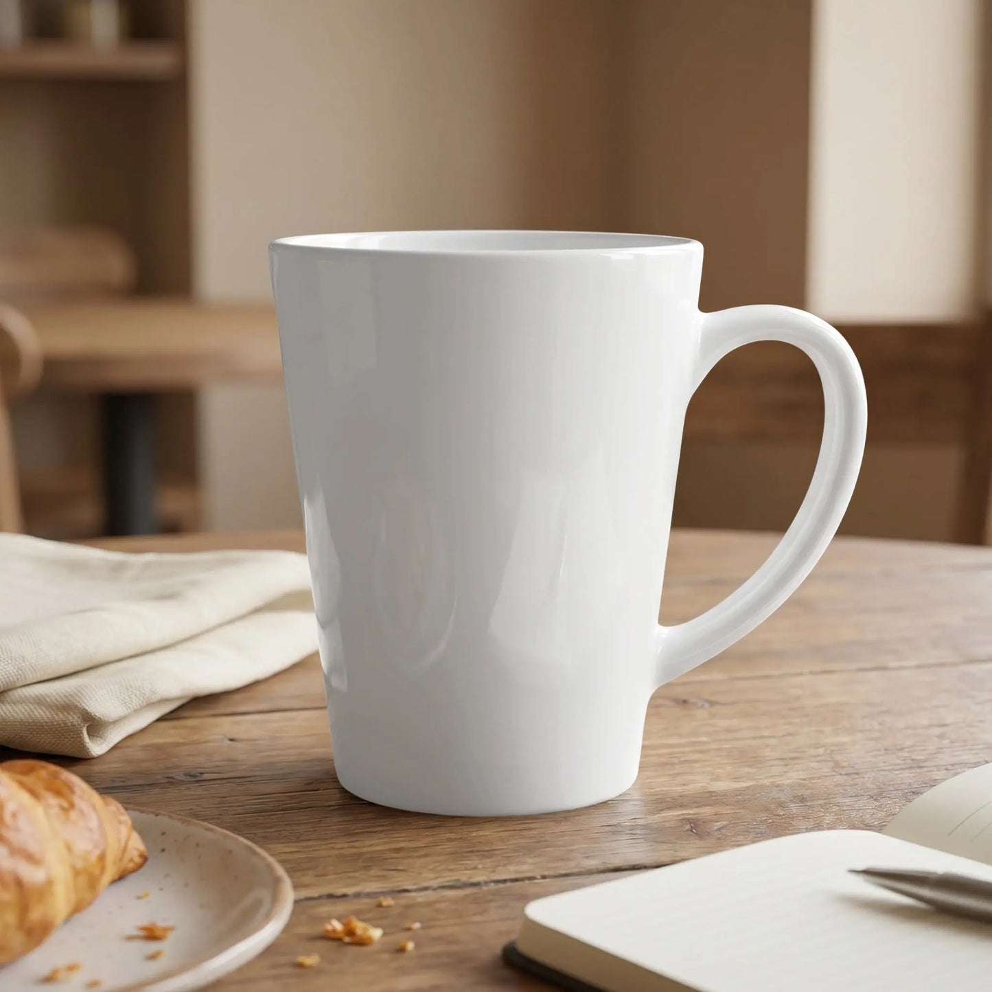 White latte mug with a croissant, napkin, and open notebook on a wooden table.