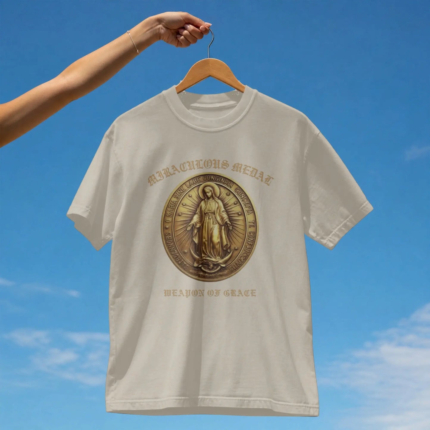Cream t-shirt with "Miraculous Medal" and "Weapon of Grace" text and a medal design.