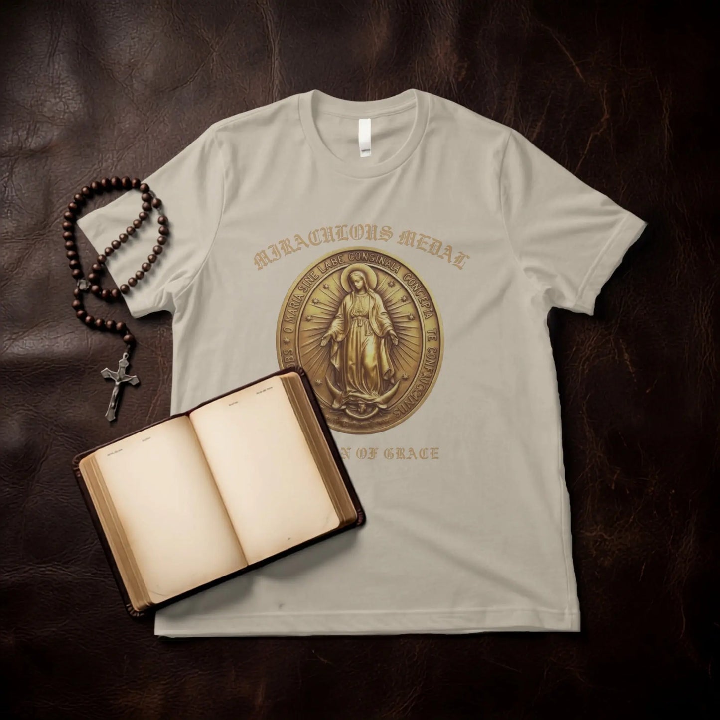 Beige t-shirt with "Miraculous Medal" text and image, rosary, and open book.