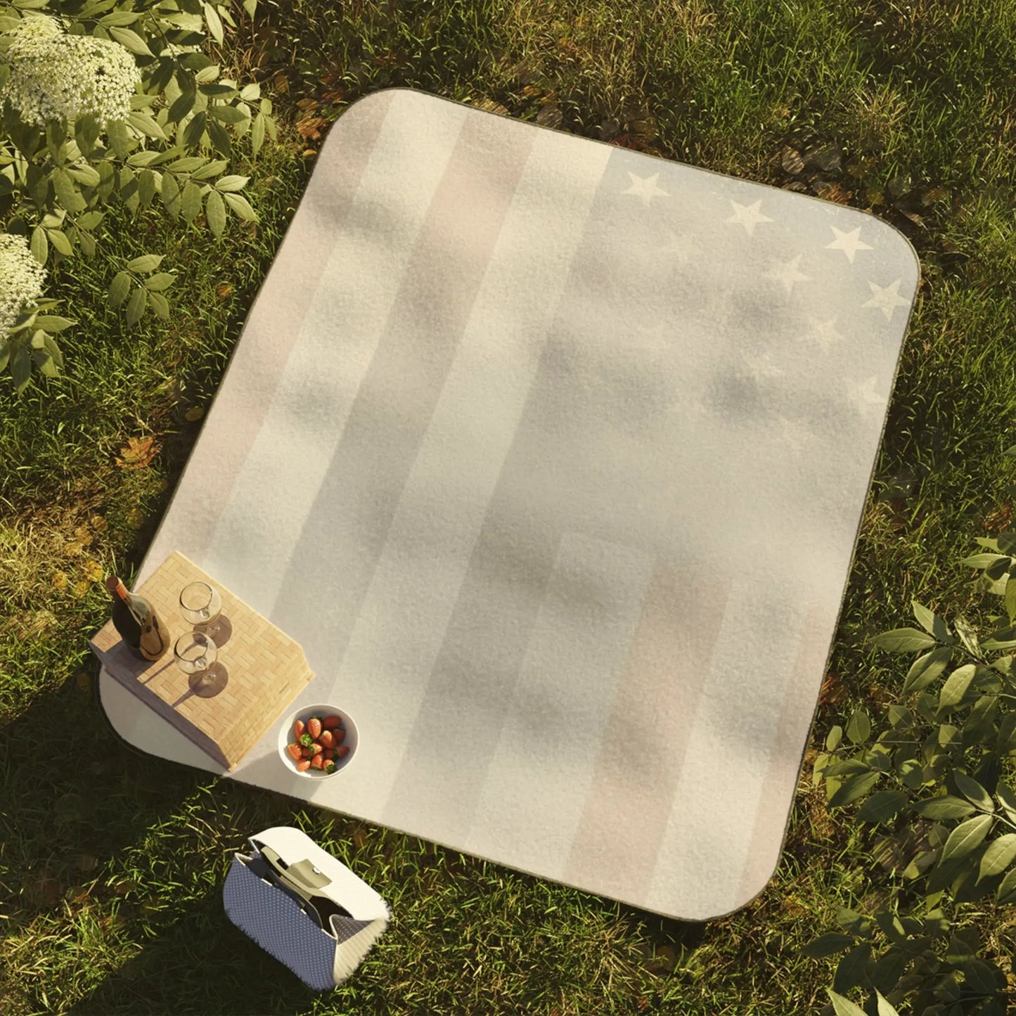 Picnic blanket with American flag design on grass with drinks and strawberries.