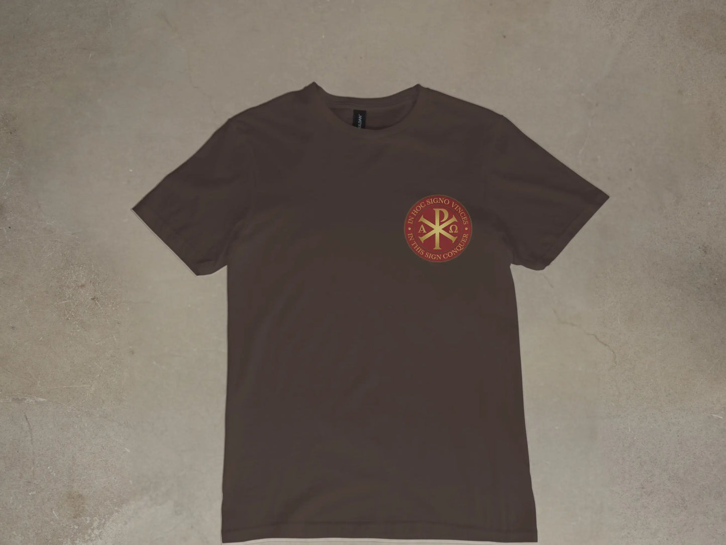 Brown t-shirt with round emblem featuring Chi Rho symbol and Latin/English text.