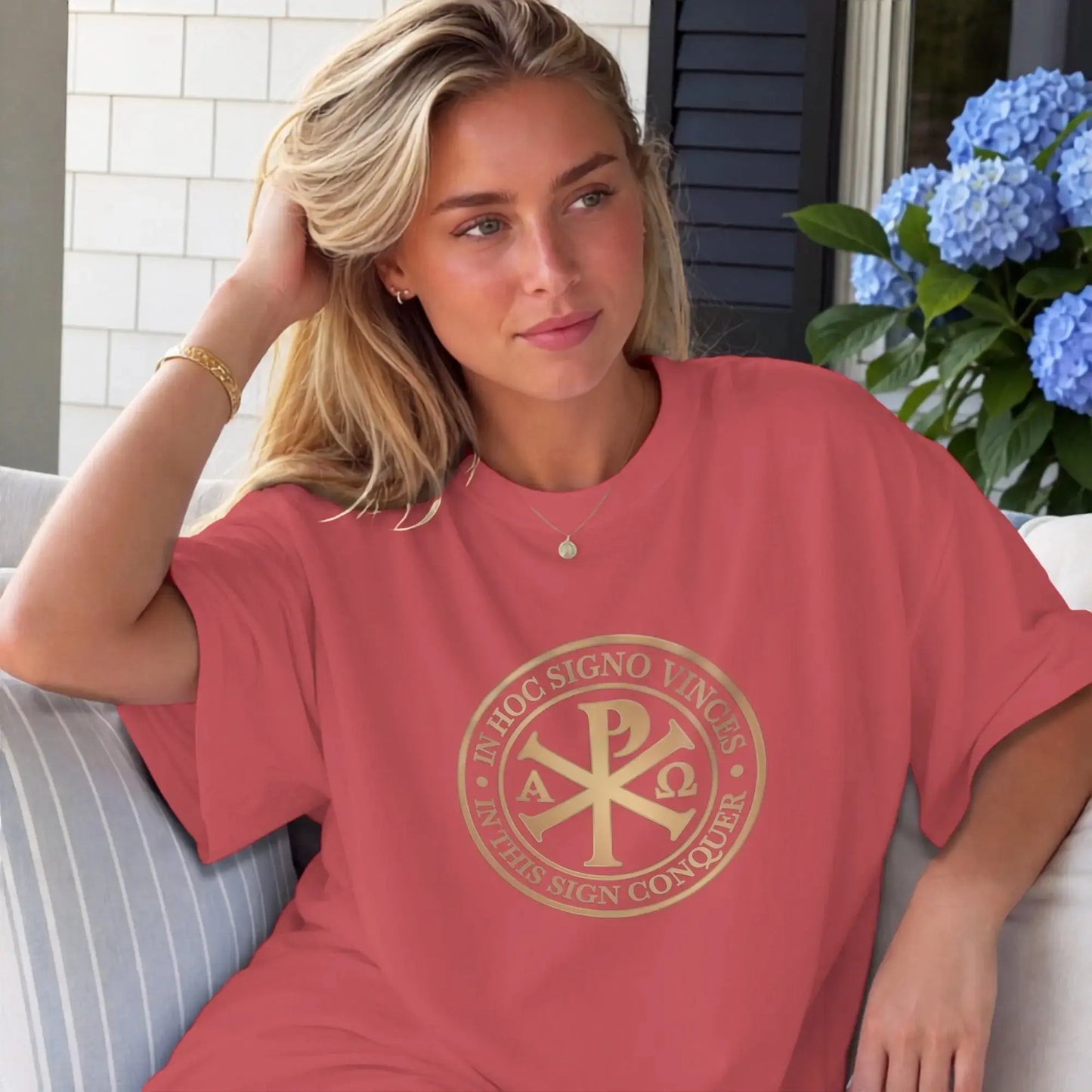 Woman wearing coral t-shirt with gold Chi Rho emblem and Latin text.
