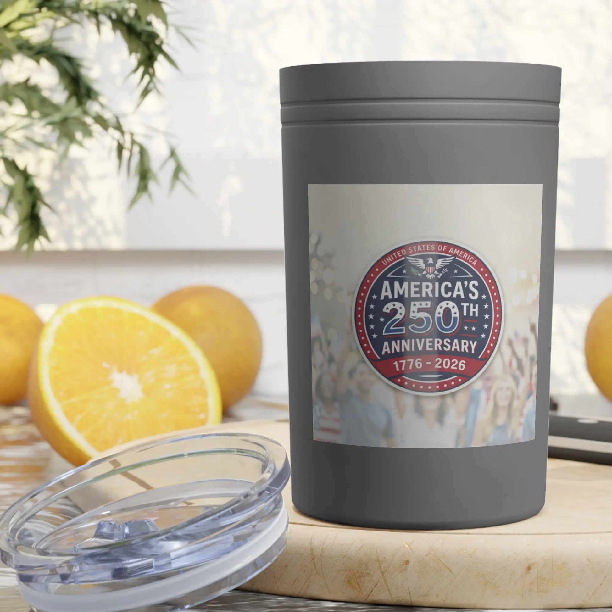 Gray tumbler with America's 250th Anniversary logo, near oranges.