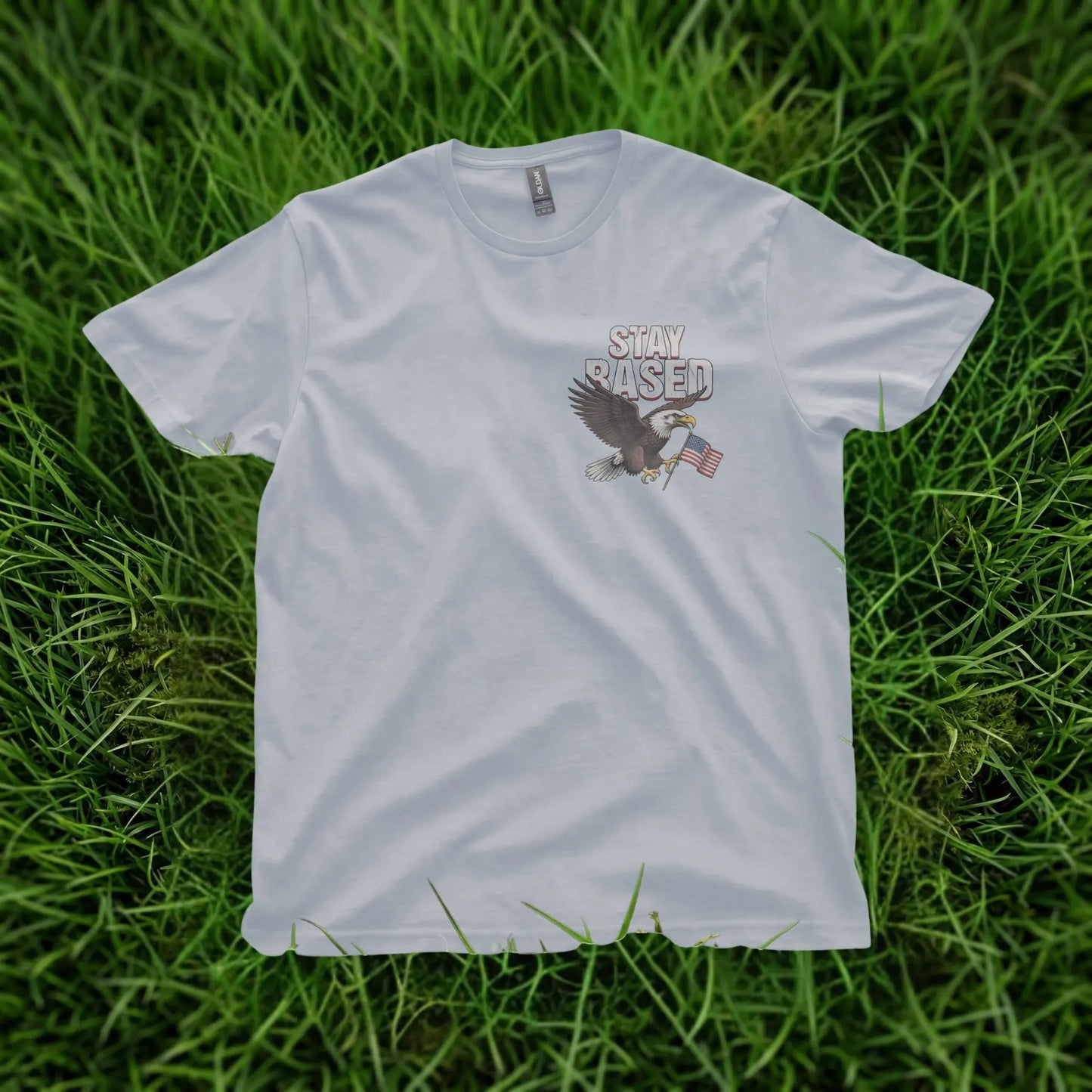 Light blue t-shirt with eagle graphic and "STAY BASED" text on grass.
