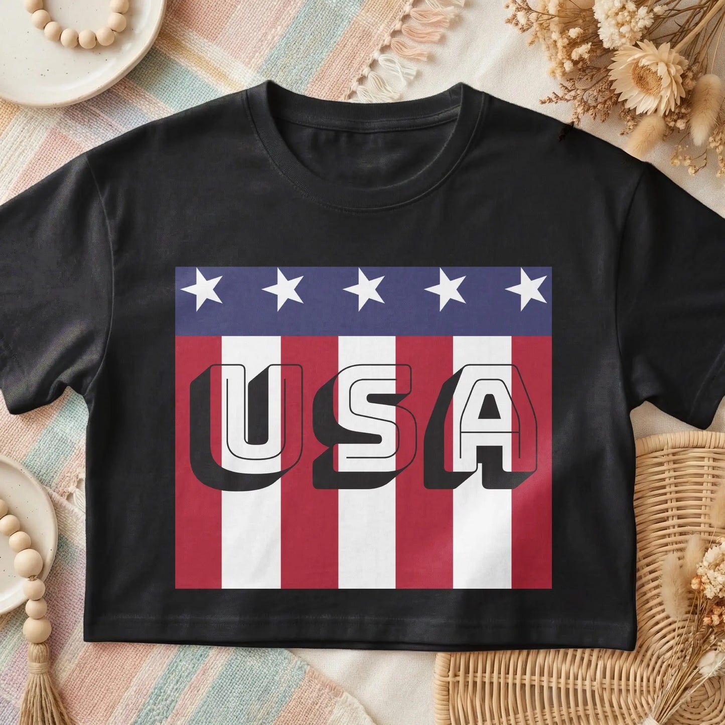 Black t-shirt with bold white "USA" text over a red and white striped background with stars.