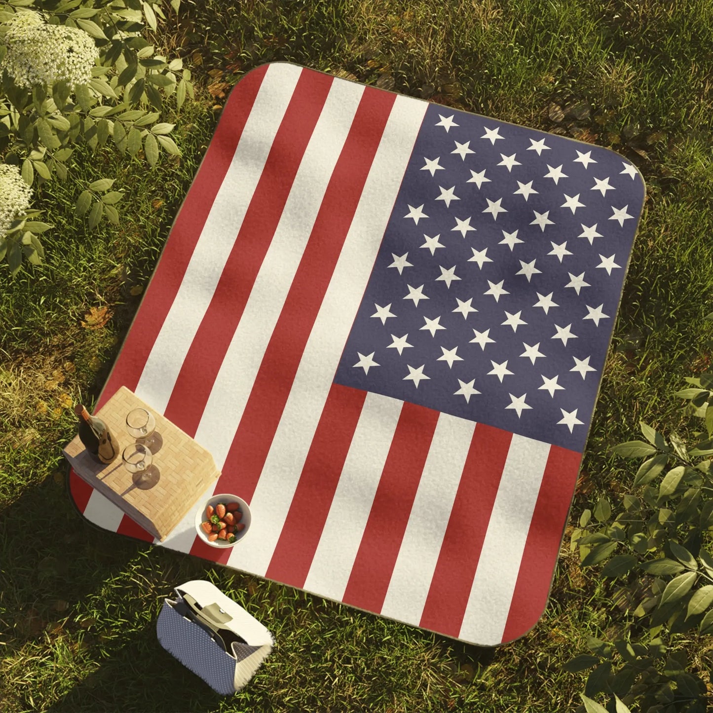 Picnic blanket with American flag design on grass with snacks and drinks.
